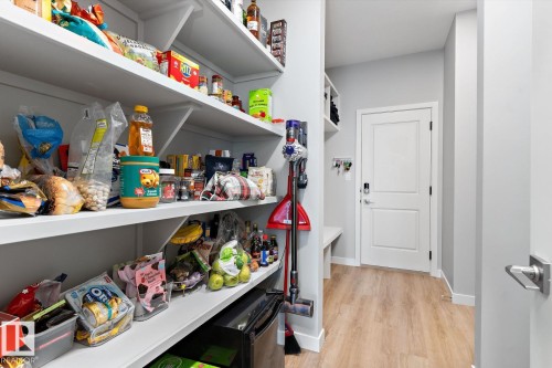 Built-in pantry shelving, white two-panel interior door, light wood-finish flooring, white baseboards, and matte silver door hardware - 3241 Kulay Way Sw, Edmonton, AB - Indoor With Storage