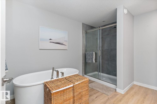 Freestanding bathtub with brushed nickel fixtures, glass-enclosed shower with dark tile surround, and wood-finish flooring - 3241 Kulay Way Sw, Edmonton, AB - Indoor Photo Showing Bathroom