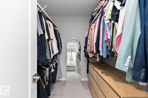 Walk-through closet featuring wood-finish built-in drawers, carpeted flooring, and an arched doorway - 3241 Kulay Way Sw, Edmonton, AB - Indoor With Storage