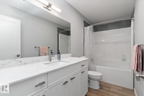 White vanity with integrated sink, stone-finish countertop, and wood-finish flooring - 3241 Kulay Way Sw, Edmonton, AB - Indoor Photo Showing Bathroom