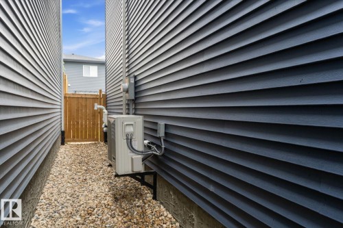 Dark horizontal siding, gravel pathway, wooden privacy fence, exterior mounted utility boxes, and an HVAC unit - 3241 Kulay Way Sw, Edmonton, AB - Outdoor