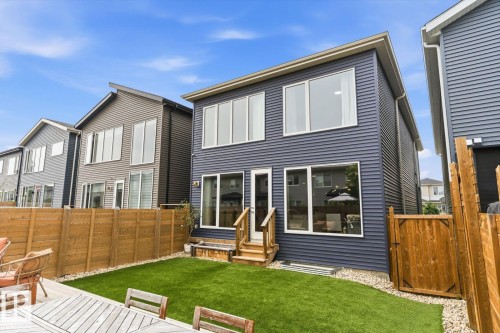 Two-story exterior with dark blue siding, large windows, a wooden deck, artificial turf, and a wood privacy fence - 3241 Kulay Way Sw, Edmonton, AB - Outdoor With Deck Patio Veranda