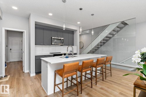 Modern kitchen featuring dark cabinetry, stainless steel appliances, a white island with an integrated sink, and wood-finish flooring - 3241 Kulay Way Sw, Edmonton, AB - Indoor Photo Showing Kitchen With Upgraded Kitchen