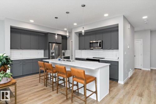 Spacious kitchen featuring gray cabinetry, stainless steel appliances, a center island with countertop seating, and wood-finish flooring - 3241 Kulay Way Sw, Edmonton, AB - Indoor Photo Showing Kitchen With Stainless Steel Kitchen With Upgraded Kitchen
