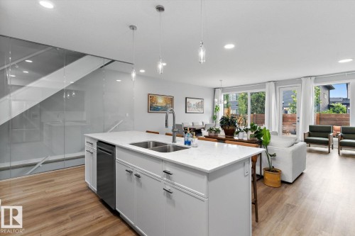 Kitchen island with a white countertop and integrated double sink, wood-finish flooring, glass panel stairway, recessed lighting, and large windows - 3241 Kulay Way Sw, Edmonton, AB - Indoor Photo Showing Other Room