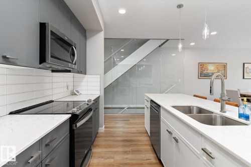 Kitchen featuring stainless steel appliances, white subway tile backsplash, white countertops, and wood-finish flooring - 3241 Kulay Way Sw, Edmonton, AB - Indoor Photo Showing Kitchen With Double Sink With Upgraded Kitchen