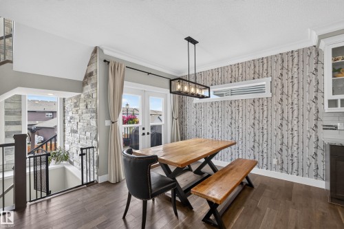 Wood-finish flooring, accent wall with stone detailing, decorative wall covering, French doors, and an exposed beam chandelier - 1399 Graydon Hill Way Sw, Edmonton, AB - Indoor Photo Showing Other Room With Fireplace