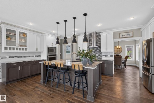 Spacious kitchen featuring an expansive center island, integrated stainless steel appliances, wood-finish flooring, two-tone cabinetry, and pendant lighting - 1399 Graydon Hill Way Sw, Edmonton, AB - Indoor Photo Showing Kitchen With Upgraded Kitchen