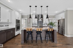 Kitchen featuring a large island with stone countertop, stainless steel appliances, wood-finish flooring, and pendant lighting - 