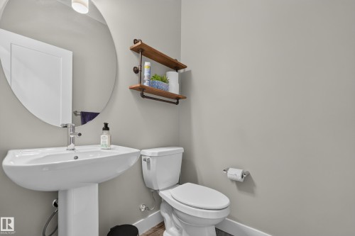 Pedestal sink with chrome faucet, round wall mirror, and wall-mounted shelving with pipe-style supports - 1399 Graydon Hill Way Sw, Edmonton, AB - Indoor Photo Showing Bathroom