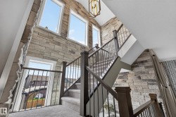 Stone accent wall with multiple windows, carpeted staircase, dark wood railings with metal spindles, and a geometric pendant light fixture - 