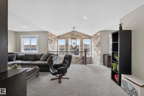Carpeted loft space featuring an exposed stone accent wall, vaulted ceiling, and built-in shelving - 1399 Graydon Hill Way Sw, Edmonton, AB - Indoor Photo Showing Living Room
