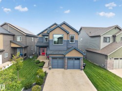 Two-story exterior with multi-toned siding, a double garage, paved driveway, and mature landscaping - 