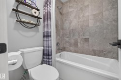 Bathtub with tiled surround, chrome shower fixtures, and white toilet - 