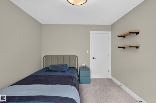 Neutral wall color, wall-mounted shelving, modern flush-mount ceiling light, white door with dark hardware, and light-toned carpeting - 1399 Graydon Hill Way Sw, Edmonton, AB - Indoor Photo Showing Bedroom