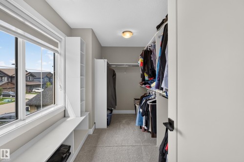 Walk-in closet featuring carpet flooring, built-in shelving, hanging rods, and a window with a built-in bench - 1399 Graydon Hill Way Sw, Edmonton, AB - Indoor