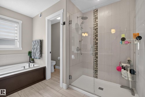 Fully tiled shower with a glass enclosure, rain showerhead, and a decorative tile accent strip - 1399 Graydon Hill Way Sw, Edmonton, AB - Indoor Photo Showing Bathroom