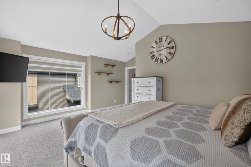 Vaulted ceiling with an industrial-style chandelier, large window with white trim, wall-mounted shelving, and carpet flooring - 1399 Graydon Hill Way Sw, Edmonton, AB - Indoor Photo Showing Bedroom