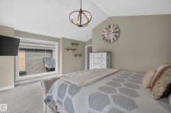 Vaulted ceiling with an industrial-style chandelier, large window with white trim, wall-mounted shelving, and carpet flooring - 