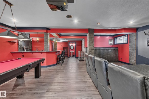 Spacious recreation room featuring wood-finish flooring, a built-in wet bar with pendant lighting, and stone veneer accents - 1399 Graydon Hill Way Sw, Edmonton, AB - Indoor Photo Showing Other Room