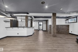 Spacious finished lower level featuring wood-finish flooring, stone-veneer accents, recessed lighting, a built-in wet bar, and a powder room with a pedestal sink - 