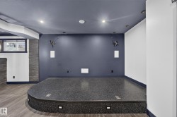 Built-in platform with integrated lighting, wood-finish flooring, recessed ceiling lights, and accent wall with stone-finish columns - 