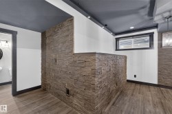 Textured stone wall accents, wood-finish flooring, recessed lighting, and a window with dark trim - 
