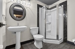 Pedestal sink with chrome faucet, round decorative mirror, corner shower enclosure with built-in shelving, wood-finish flooring, and subway tile accents - 