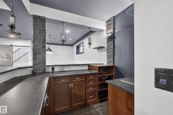 Lower-level built-in cabinetry with dark countertops, stone-clad architectural columns, and pendant lighting - 