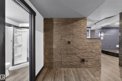 Stone accent wall, wood-finish flooring, full bathroom with shower, and contemporary pendant lighting - 