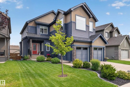 Two-story home with a two-car garage, stone accents, mature landscaping, and a red entry door - 1399 Graydon Hill Way Sw, Edmonton, AB - Outdoor With Facade
