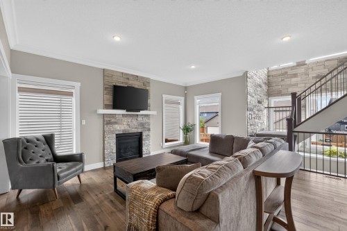 Living room featuring a stone-clad fireplace with a white mantel, wood-finish flooring, recessed lighting, and a multi-level staircase with iron balusters - 1399 Graydon Hill Way Sw, Edmonton, AB - Indoor Photo Showing Living Room With Fireplace