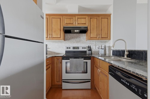 Kitchen featuring wood-finish cabinetry, stone countertops, and a tile backsplash - #9 13215 153 Av Nw, Edmonton, AB - Indoor Photo Showing Kitchen With Double Sink