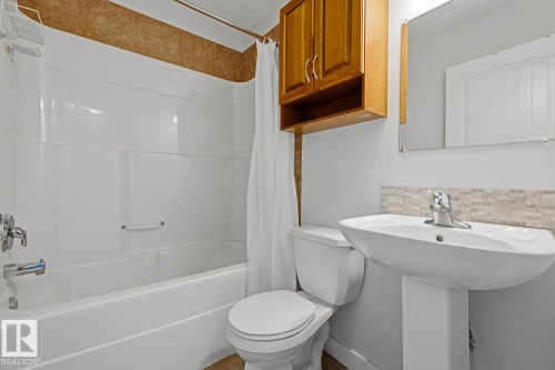 White pedestal sink with chrome faucet, complemented by a mosaic tile backsplash - #9 13215 153 Av Nw, Edmonton, AB - Indoor Photo Showing Bathroom