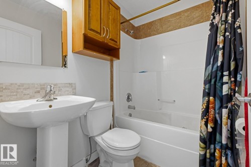 Pedestal sink with a chrome faucet, toilet, and bathtub with a white surround - #9 13215 153 Av Nw, Edmonton, AB - Indoor Photo Showing Bathroom