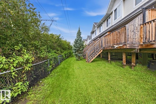 Expansive green space featuring a chain-link fence, mature trees, and a multi-level wood deck - #9 13215 153 Av Nw, Edmonton, AB - Outdoor With Deck Patio Veranda