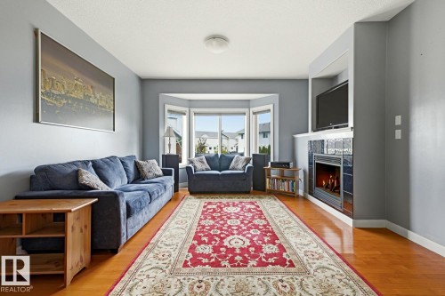 Hardwood flooring throughout, a gas fireplace with tile surround, built-in media niche, and a bay window - #9 13215 153 Av Nw, Edmonton, AB - Indoor Photo Showing Living Room With Fireplace