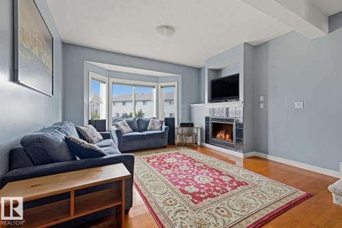 Hardwood-finish flooring, built-in fireplace with tile surround, bay window, and recessed media niche - #9 13215 153 Av Nw, Edmonton, AB - Indoor Photo Showing Living Room With Fireplace