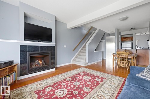 Hardwood-style flooring throughout, a tiled fireplace with mantel, and a built-in kitchen island - #9 13215 153 Av Nw, Edmonton, AB - Indoor Photo Showing Living Room With Fireplace