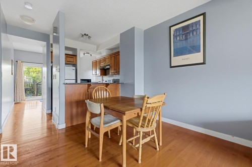 Wood-finish flooring throughout, kitchen with wood cabinetry and built-in appliances, breakfast bar, and a balcony with metal railing - #9 13215 153 Av Nw, Edmonton, AB - Indoor Photo Showing Dining Room