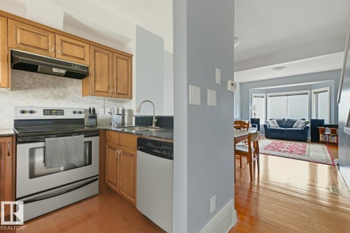 Kitchen featuring wood cabinetry, stainless steel range and dishwasher, granite countertops, and tile backsplash - #9 13215 153 Av Nw, Edmonton, AB - Indoor Photo Showing Kitchen