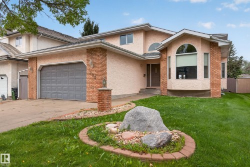 Stucco exterior with brick accents, arched and rectangular windows, attached two-car garage, concrete driveway, and a front yard with a rock garden - 306 Twin Brooks Drive Nw, Edmonton, AB 