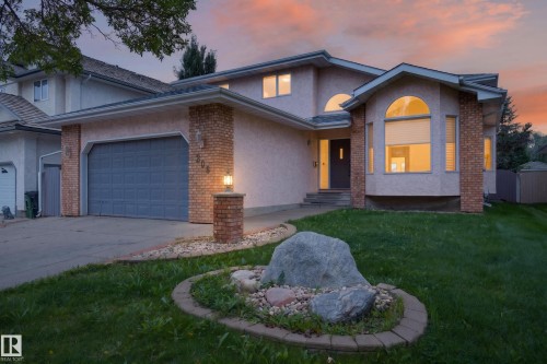 Stucco exterior with brick accents, arched windows, an attached garage, and a landscaped front yard with a rock feature - 306 Twin Brooks Drive Nw, Edmonton, AB 