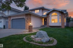 Stucco exterior with brick accents, arched windows, an attached garage, and a landscaped front yard with a rock feature - 