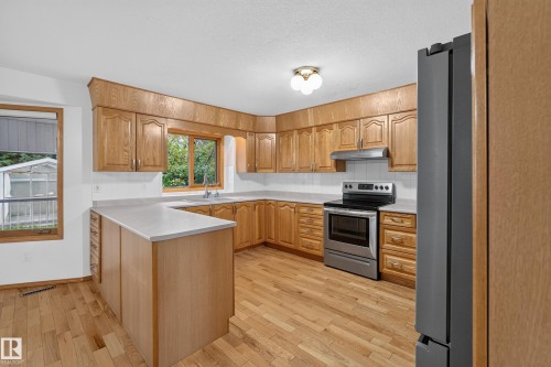 Kitchen featuring wood cabinetry, light-toned countertops, stainless steel appliances, and wood-finish flooring - 306 Twin Brooks Drive Nw, Edmonton, AB 