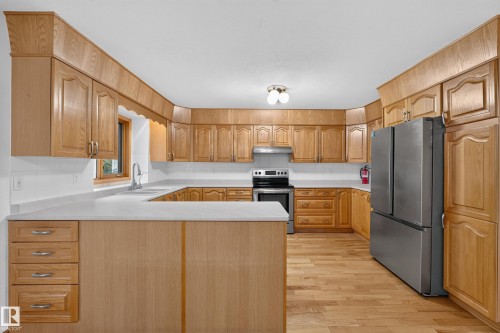 U-shaped kitchen with wood-finish cabinetry, white countertops, and stainless steel appliances - 306 Twin Brooks Drive Nw, Edmonton, AB 