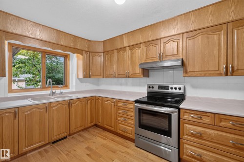 Wood-finish cabinetry, stainless steel range, and light countertops with a tile backsplash - 306 Twin Brooks Drive Nw, Edmonton, AB 