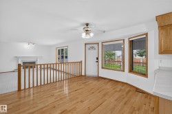 Hardwood flooring, bay windows, ceiling fan, white entry door with decorative glass, and a white fireplace - 