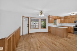 Wood-finish flooring throughout, kitchen with light wood cabinetry and light countertops, stainless steel range, and a ceiling fan with light fixture - 