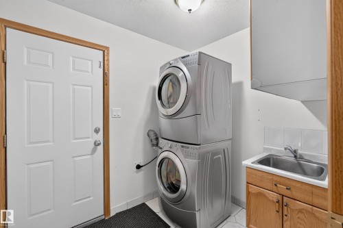 Dedicated laundry area featuring a stacked washer and dryer, utility sink with a faucet, and white tile backsplash - 306 Twin Brooks Drive Nw, Edmonton, AB 